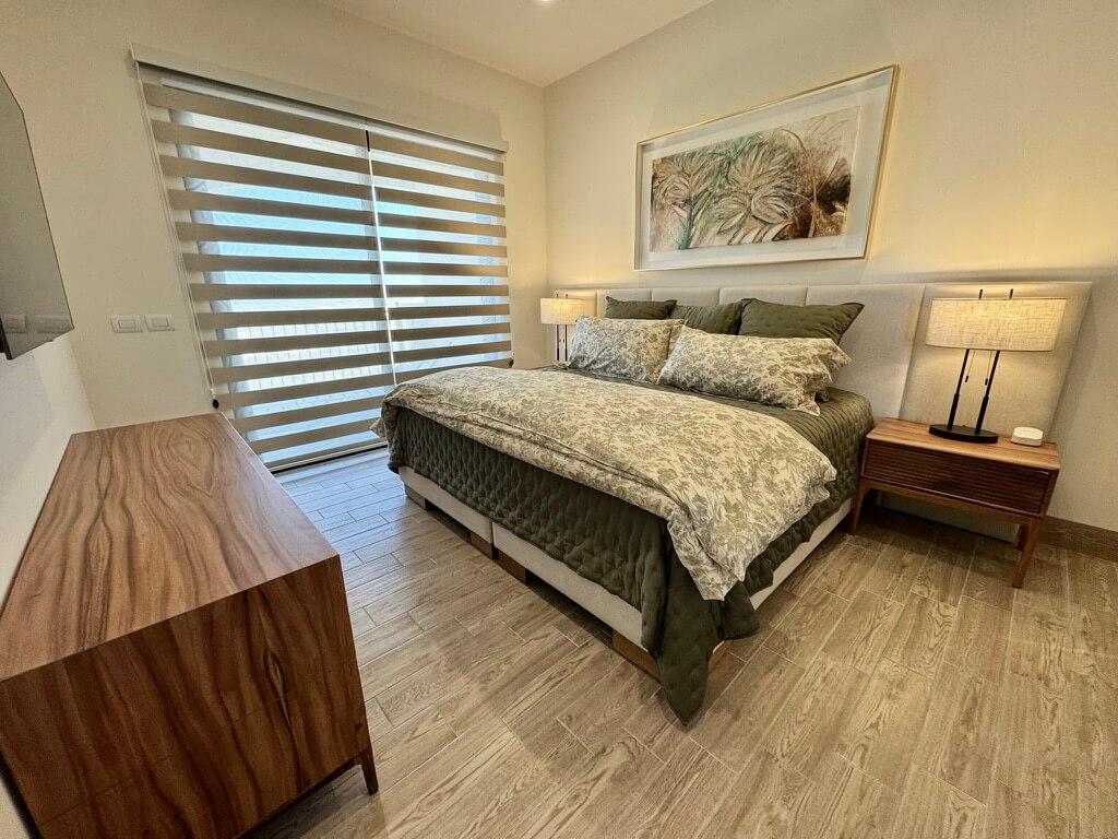 Modern Los Cabos condo bedroom with upholstered bed, wood nightstands, and walnut credenza